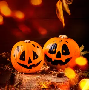 Zwei orangene Kürbisse auf Tisch mit schwarz aufgemaltem gruseligen Gesicht, Motiv für Halloween-Einladungskarten