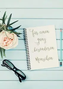 Ein Spruch zum Muttertag auf einem Notizbuch: "Für einen ganz besonderen Menschen." Daneben steht ein Blumenstrauß