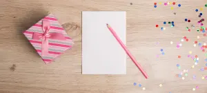Geschenkschachtel mit Schleife, daneben ein Blatt Papier und ein Stift