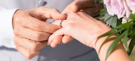 Mann steckt Frau einen Ring in Gold an die Hand, die Hochzeitseinladungen sind hoffentlich verschickt