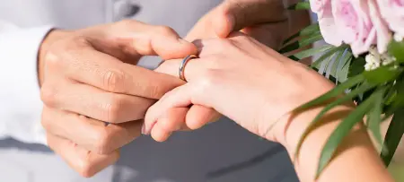 Mann steckt Frau einen Ring in Gold an die Hand, die Hochzeitseinladungen sind hoffentlich verschickt