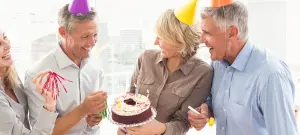 Mann und Frau feiern Geburtstag mit bunten Partyhüten und Kuchen