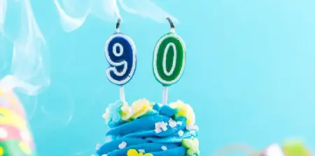 90 in Kerzenform auf Torte, die ausgeblasen sind, in Blautönen gehalten mit bunten Akzenten