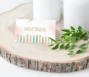 Schöne Platzkarte mit Namen "Hendrick" und bunten Kerzen als Motiv, als Tischdekoration mit weißen Kerzen im Hintergrund