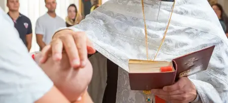Baby wird gesegnet in Hand des Geistlichen auf Kopf des Kindes