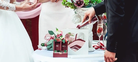 Braut und Bräutigam gestalten auf der Hochzeit einen Herzaufsteller mit rotem und weißem Sand