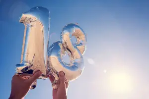zwei Luftballons in Form einer 1 und einer 8 in Silber mit Reflektionen in Gold werden von zwei Händen gehalten und als Hintergrund dient der blaue Himmel