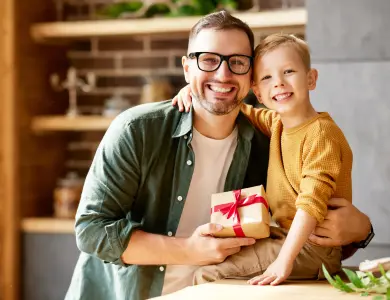 Ein Papa hält ein Vatertagsgeschenk in der Hand und umarmt dabei seinen Sohn. Beide sind sehr lustig und fröhlich