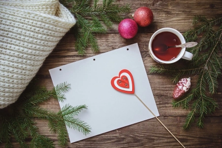 Weihnachtskarten gestalten und Ideen aufschreiben auf Papier, Holztisch mit Teetasse und Weihnachtsdeko im Hintergrund