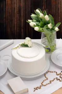 Ein weißer Kuchen und weiße Blumen, der Tisch scheint für eine Taufe, Kommunion oder Konfirmation gedeckt zu sein