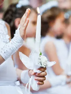 Ein Foto einer Erstkommunion: ein weißer Handschuh und eine weiße Kerze mit Blumen