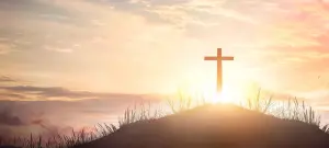 Kreuz aus Holz auf Hügel, Himmel und Sonnenstrahlen im Hintergrund