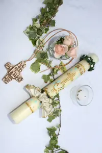 Ein Kreuz liegt neben einer weißen Kerze, daneben steht eine Rose