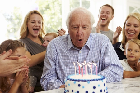 Opa bläst Kerzen auf Torte zum Geburtstag aus, Familie rund um das Geburtstagskind