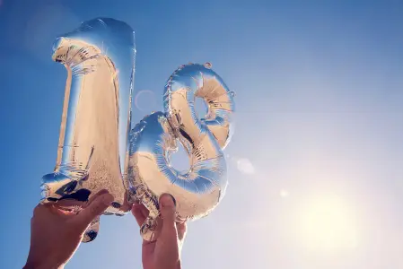 zwei Luftballons in Form einer 1 und einer 8 in Silber mit Reflektionen in Gold werden von zwei Händen gehalten und als Hintergrund dient der blaue Himmel