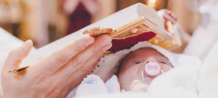 Kind bei Taufe in Kirche, im Arm fest gehalten, Bibel über Kopf des Kindes