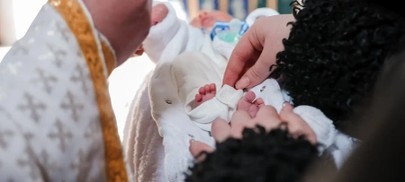 Frau hält Baby im Arm, Taufe des Kindes