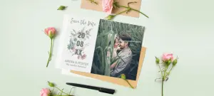 Originelle Save-the-Date Karte mit Angaben zum Hochzeitsdatum auf grüner Tischunterlage und umrahmt von Blumen