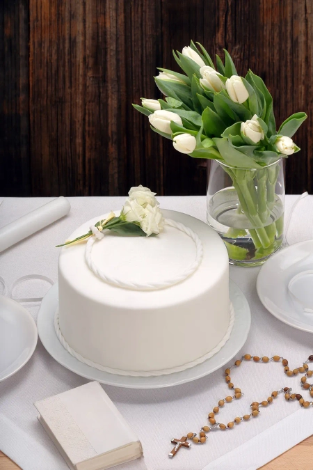 Ein weißer Kuchen und weiße Blumen, der Tisch scheint für eine Taufe, Kommunion oder Konfirmation gedeckt zu sein