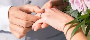 Mann steckt Frau einen Ring in Gold an die Hand, die Hochzeitseinladungen sind hoffentlich verschickt