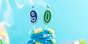 90 in Kerzenform auf Torte, die ausgeblasen sind, in Blautönen gehalten mit bunten Akzenten