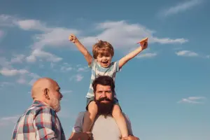Ein Vater trägt seinen Sohn auf den Schultern, der Opa steht daneben und lächelt