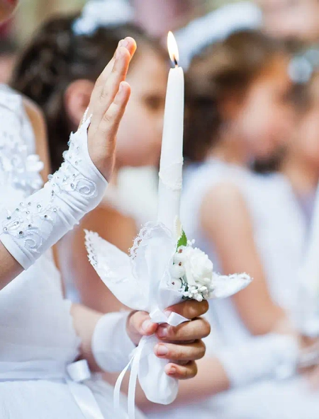 Das Bild zeigt eine christliche Kommunion, zu sehen sind weiße Handschuhe und eine weiße Kerze, typische Symbole für die Erstkommunion