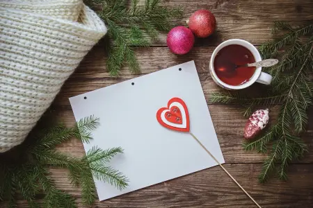 Weihnachtskarten gestalten und Ideen aufschreiben auf Papier, Holztisch mit Teetasse und Weihnachtsdeko im Hintergrund