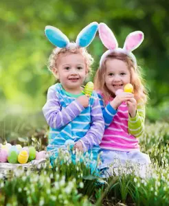 Zwei Kinder sind als bunte Osterhasen verkleidet und halten bemalte Ostereier in ihren Händen