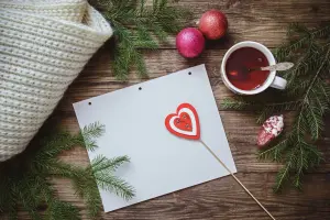 Weihnachtskarten gestalten und Ideen aufschreiben auf Papier, Holztisch mit Teetasse und Weihnachtsdeko im Hintergrund