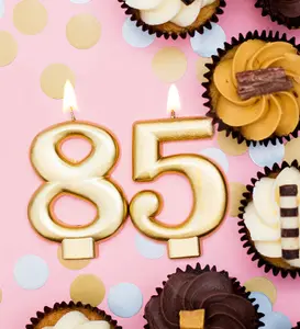 Goldene brennende 85 als Kerze auf Rosa Hintergrund, mit Konfetti und Cupcakes als Design für Einladungskarte zum runden Geburtstag