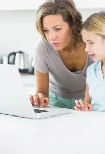 Mutter und Kind schauen gemeinsam auf einen Computer Bildschirm und gestalten Menükarten für die Konfirmation