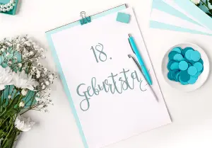 Einladungskarten zum 18. Geburtstag auf Schreibtisch mit türkisfarbenen Akzenten in der Einladung aber auch auf dem Arbeitsbereich