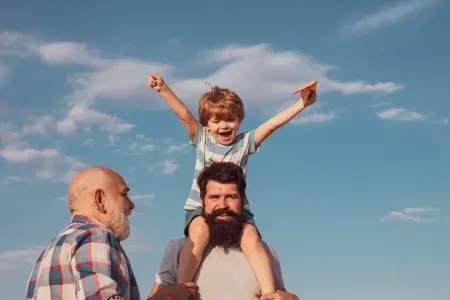 Ein Vater trägt seinen Sohn auf den Schultern, der Opa steht daneben und lächelt