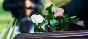 Stille Trauerfeier, dunkler Sarg mit weißer Rose, trauernde