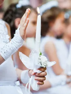 Das Bild zeigt eine christliche Kommunion, zu sehen sind weiße Handschuhe und eine weiße Kerze, typische Symbole für die Erstkommunion