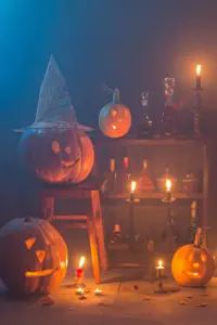 Halloween Kürbisse in orange in gruseligem Zimmer mit Kerzen und Hexenhut und Spinnen