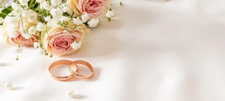 weißer Untergrund mit Hochzeitsringen in Gold und weißen Rosen