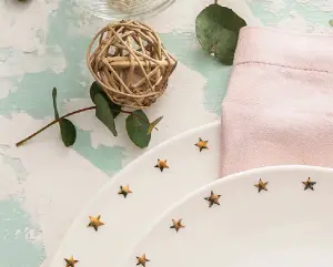 Weiße Teller mit goldenen Sternchen verziert und schönen Blumen als Tischdekoration zum Geburtstag oder zur Kommunion und Konfirmation
