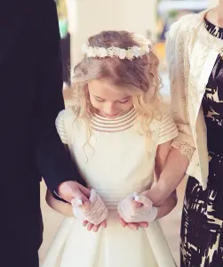 Ein Mädchen wird von ihren Eltern gehalten, sie trägt ein weißes Kleid zu ihrer Kommunion