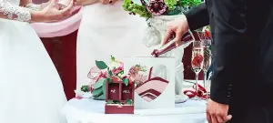 Braut und Bräutigam gestalten auf der Hochzeit einen Herzaufsteller mit rotem und weißem Sand