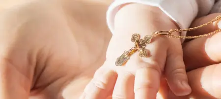 Babyhand mit goldener Kette und Kreuz