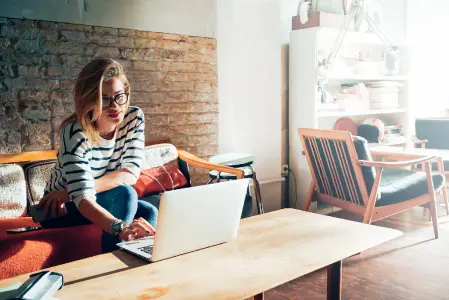 Teenager gestaltet Einladungskarten für ihren Geburtstag am Laptop, sitzt auf cooler Couch