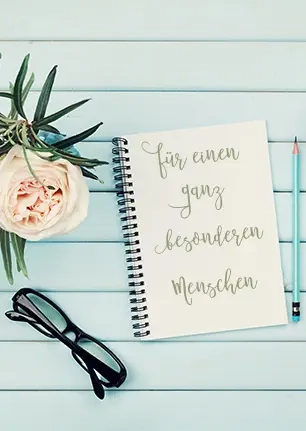 Ein Spruch zum Muttertag auf einem Notizbuch: "Für einen ganz besonderen Menschen." Daneben steht ein Blumenstrauß