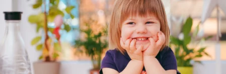 Fröhliches Kindergartenkind lächelt und hält sich die Hände an die Backen